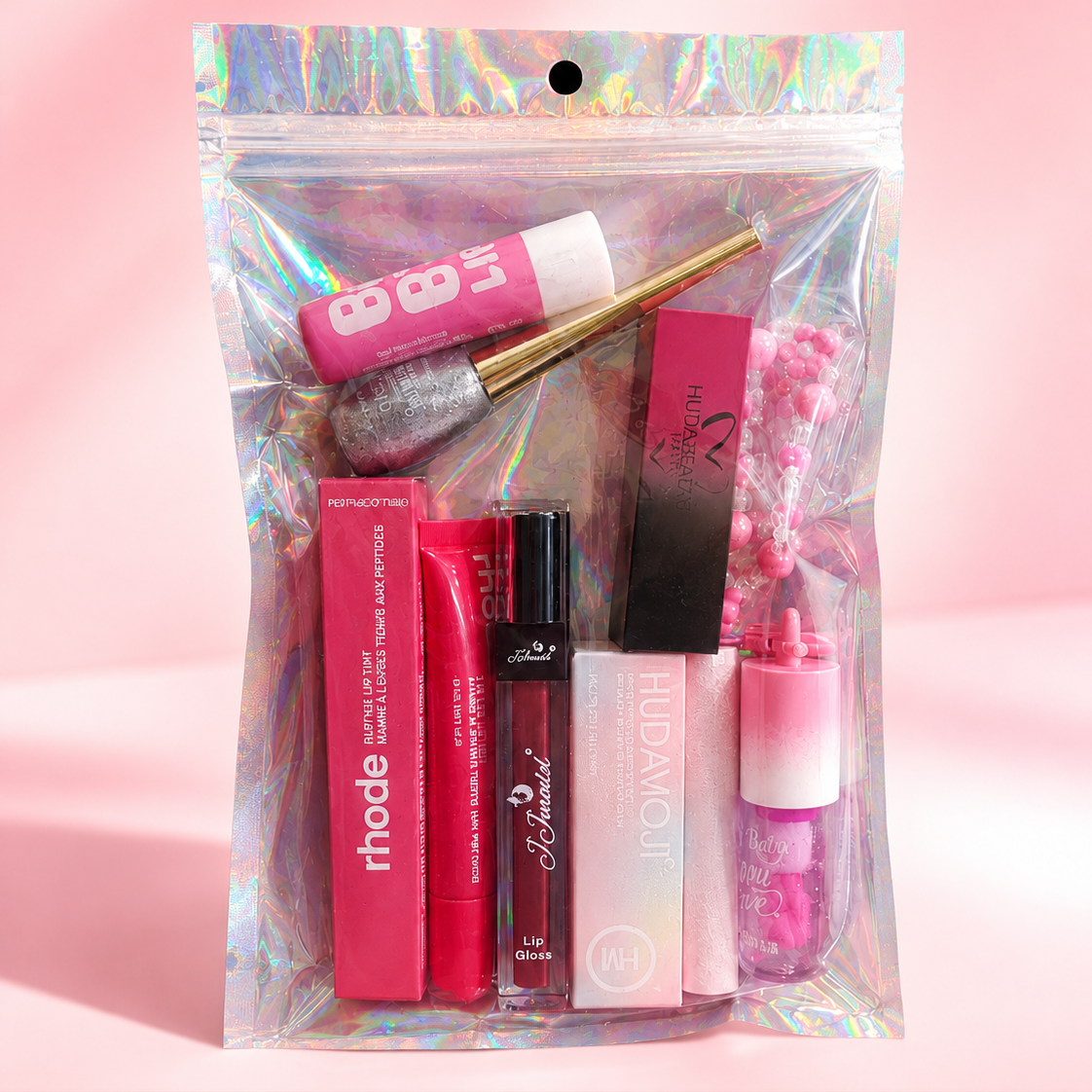 A clear holographic zip pouch containing assorted pink and red cosmetics, including lip gloss, lipsticks, and a cream product, photographed on a soft pink background. The brand name ECLAT BY TUBA appears in the top left, and social media/store details are shown along the bottom.