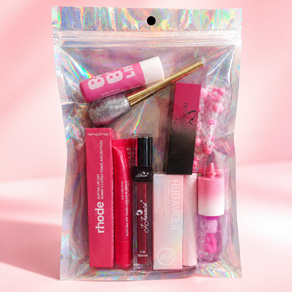 A clear holographic zip pouch containing assorted pink and red cosmetics, including lip gloss, lipsticks, and a cream product, photographed on a soft pink background. The brand name ECLAT BY TUBA appears in the top left, and social media/store details are shown along the bottom.