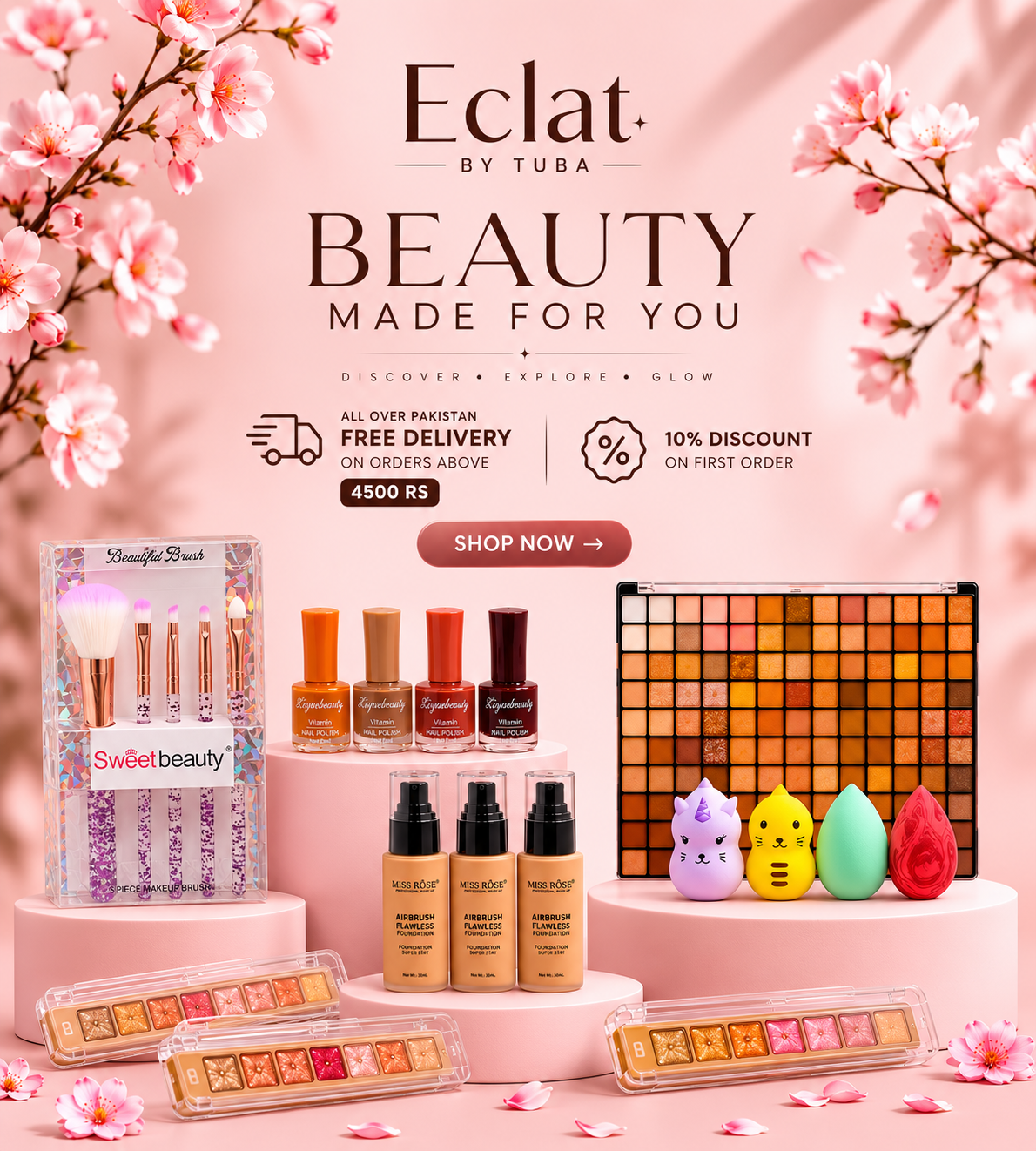 A promotional display of multiple cosmetic products arranged on pink pedestals against a soft pink background with cherry blossom branches. Visible items include an eyeshadow palette, makeup brushes in a clear case, several small bottles and jars, and three small character-shaped makeup pots.